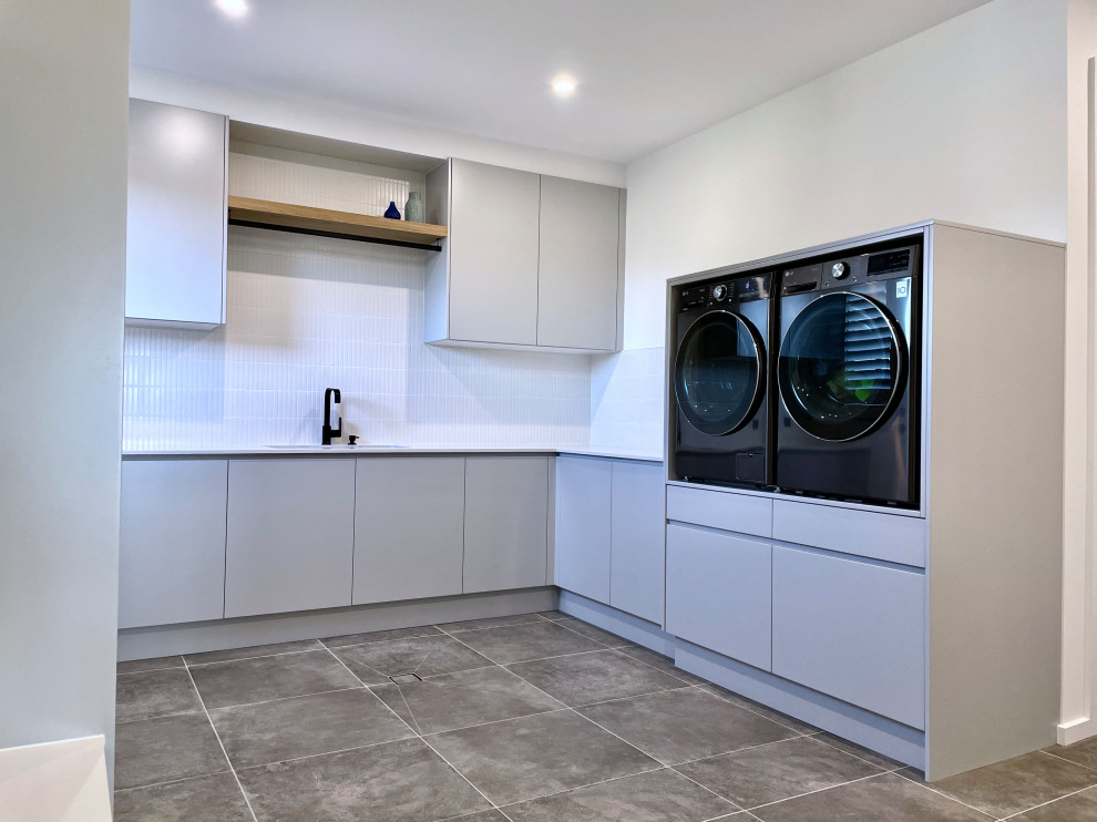 Exempel på en mycket stor modern vita u-formad vitt tvättstuga enbart för tvätt, med en undermonterad diskho, släta luckor, grå skåp, bänkskiva i kvarts, vitt stänkskydd, stänkskydd i keramik, vita väggar, klinkergolv i keramik, en tvättmaskin och torktumlare bredvid varandra och grått golv