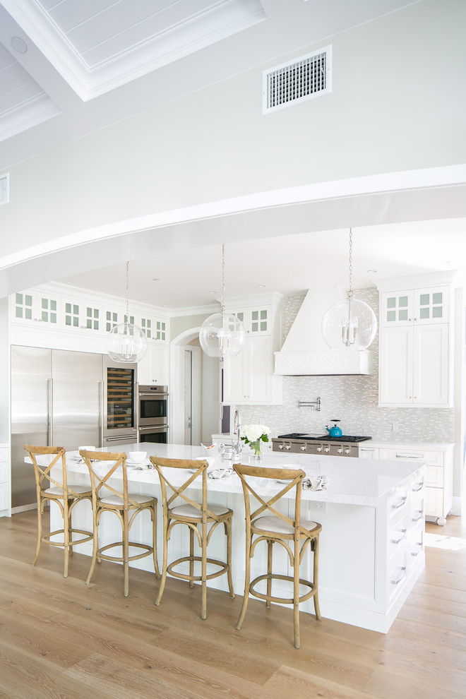 Design ideas for a transitional l-shaped kitchen in Orange County with shaker cabinets, white cabinets, white splashback, matchstick tile splashback, stainless steel appliances, medium hardwood floors, with island, brown floor and white benchtop.