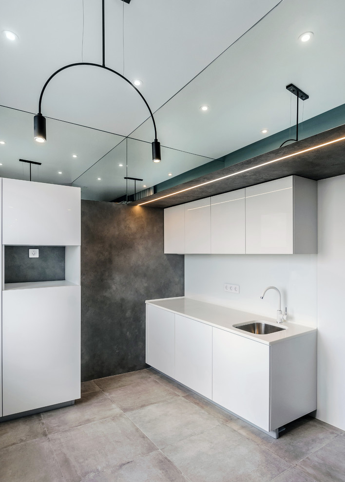 This is an example of a small industrial single-wall open plan kitchen in Novosibirsk with an undermount sink, flat-panel cabinets, white cabinets, solid surface benchtops, white splashback, glass sheet splashback, porcelain floors, no island, grey floor and white benchtop.
