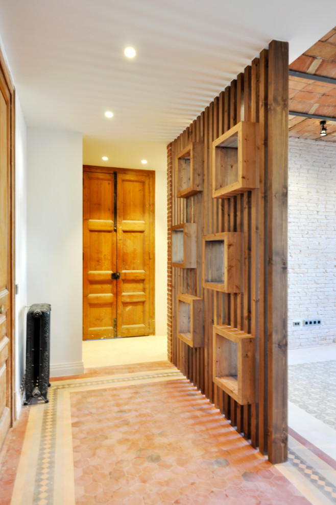 This is an example of a large modern entry hall in Barcelona with white walls, ceramic floors, a single front door, a metal front door, grey floor, vaulted and brick walls.