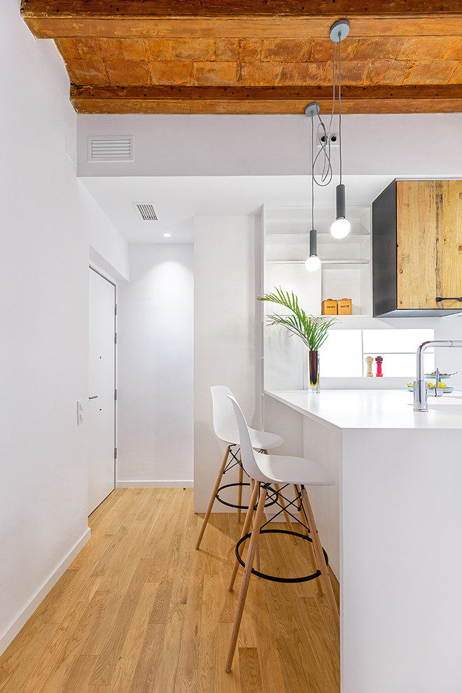 Photo of a modern separate kitchen in Barcelona with an integrated sink, flat-panel cabinets, white cabinets, light hardwood floors, a peninsula, beige floor and white benchtop.