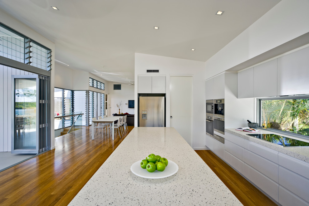 Photo of a mid-sized contemporary galley eat-in kitchen in Brisbane with an undermount sink, white cabinets, quartz benchtops, glass sheet splashback, stainless steel appliances, light hardwood floors and with island.