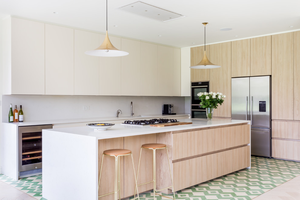 This is an example of a scandinavian kitchen in London with a single-bowl sink, flat-panel cabinets, light wood cabinets, white splashback, stainless steel appliances, with island, multi-coloured floor and white benchtop.