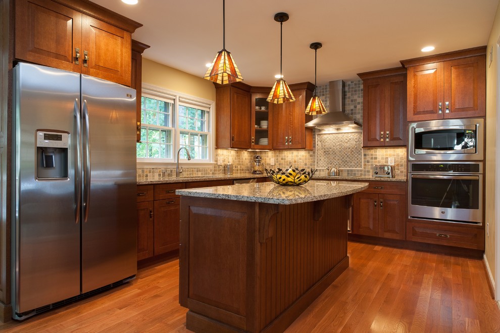 Mid-sized arts and crafts l-shaped kitchen in DC Metro with raised-panel cabinets, medium wood cabinets, stone tile splashback, stainless steel appliances, an undermount sink, granite benchtops, multi-coloured splashback, medium hardwood floors and with island.