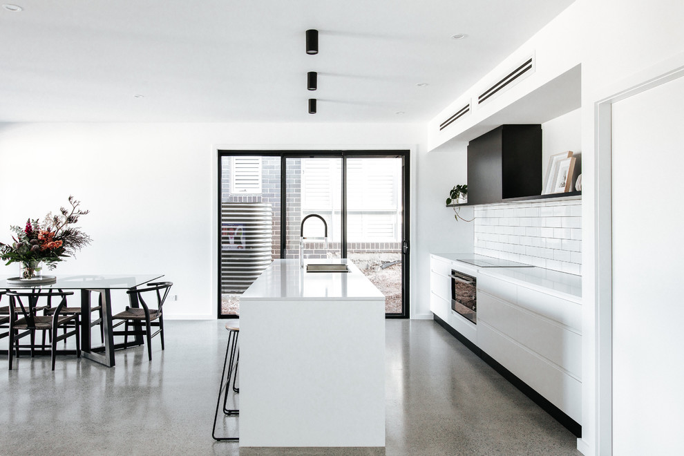 Mid-sized modern galley kitchen in Wollongong with a double-bowl sink, flat-panel cabinets, white cabinets, quartz benchtops, white splashback, ceramic splashback, stainless steel appliances, concrete floors, with island, grey floor and white benchtop.