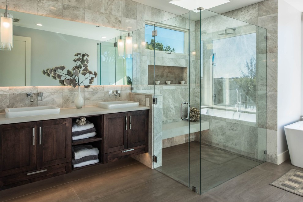 This is an example of a large transitional master bathroom in Orange County with shaker cabinets, dark wood cabinets, a freestanding tub, a curbless shower, porcelain tile, grey walls, porcelain floors and a vessel sink.