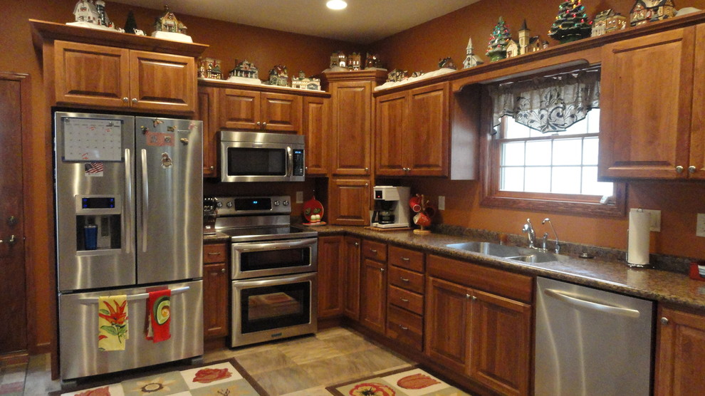 Example of a mid-sized u-shaped open concept kitchen design with an undermount sink, raised-panel cabinets, medium tone wood cabinets, laminate countertops, stainless steel appliances, orange walls and a peninsula