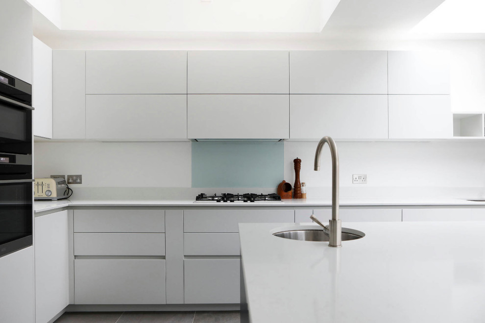 Design ideas for a large contemporary l-shaped kitchen/diner in London with a double-bowl sink, flat-panel cabinets, white cabinets, an island and white worktops.