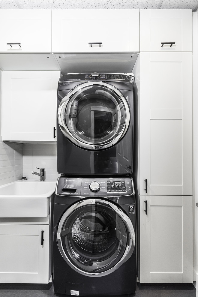 Inspiration for a mid-sized contemporary single-wall dedicated laundry room in Vancouver with a farmhouse sink, shaker cabinets, white cabinets, white walls and a stacked washer and dryer.