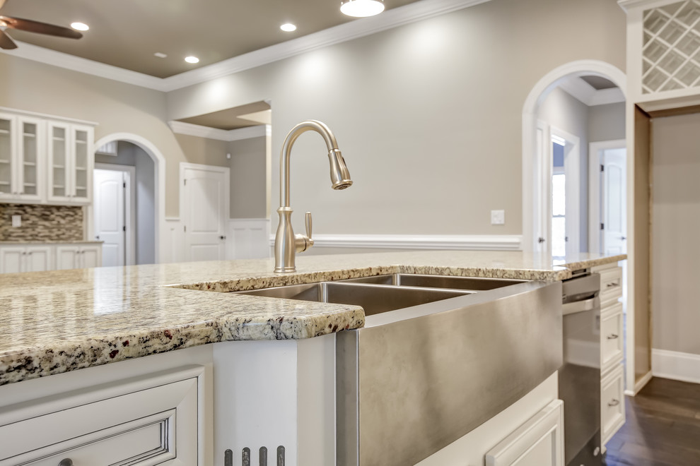Example of a mid-sized transitional l-shaped dark wood floor open concept kitchen design with a farmhouse sink, recessed-panel cabinets, white cabinets, granite countertops, beige backsplash, mosaic tile backsplash, stainless steel appliances and an island