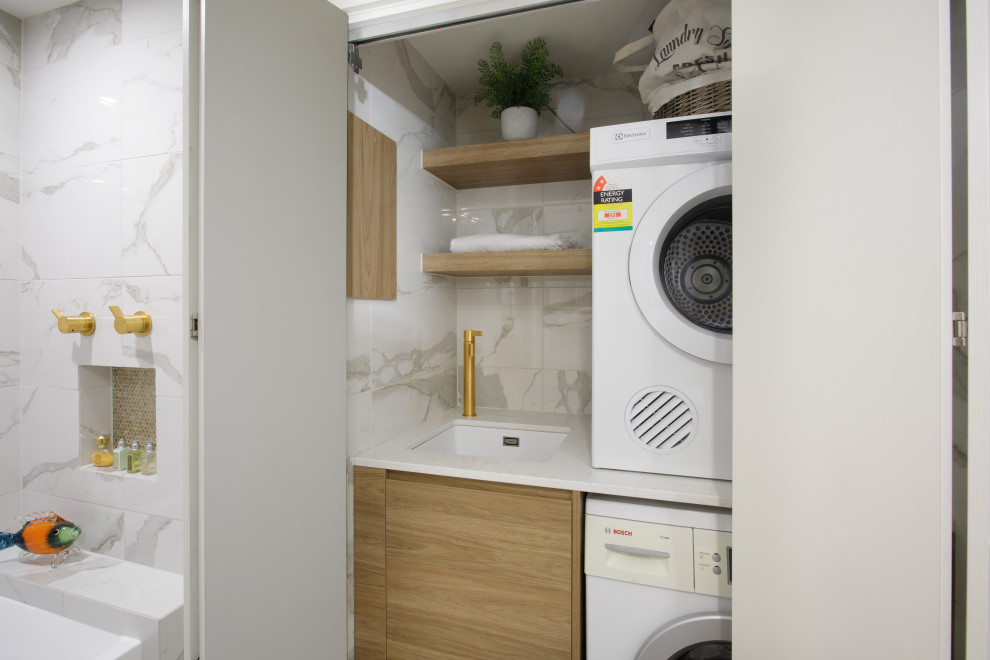 Design ideas for a small modern single-wall laundry cupboard in Brisbane with an undermount sink, medium wood cabinets, quartz benchtops, white splashback, ceramic splashback, white walls, ceramic floors, a stacked washer and dryer, white floor and white benchtop.