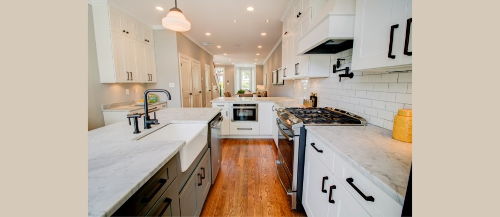 Example of a mid-sized transitional l-shaped medium tone wood floor eat-in kitchen design in DC Metro with shaker cabinets, white cabinets, an island, a farmhouse sink, marble countertops, white backsplash, subway tile backsplash and stainless steel appliances