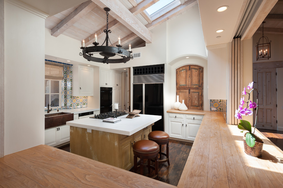 This is an example of a galley kitchen in San Diego with a farmhouse sink, raised-panel cabinets, white cabinets, multi-coloured splashback, black appliances, dark hardwood floors and with island.