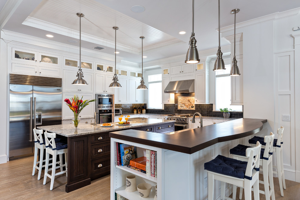 This is an example of a beach style u-shaped kitchen in Miami with shaker cabinets, white cabinets, black splashback, subway tile splashback, stainless steel appliances, medium hardwood floors and with island.