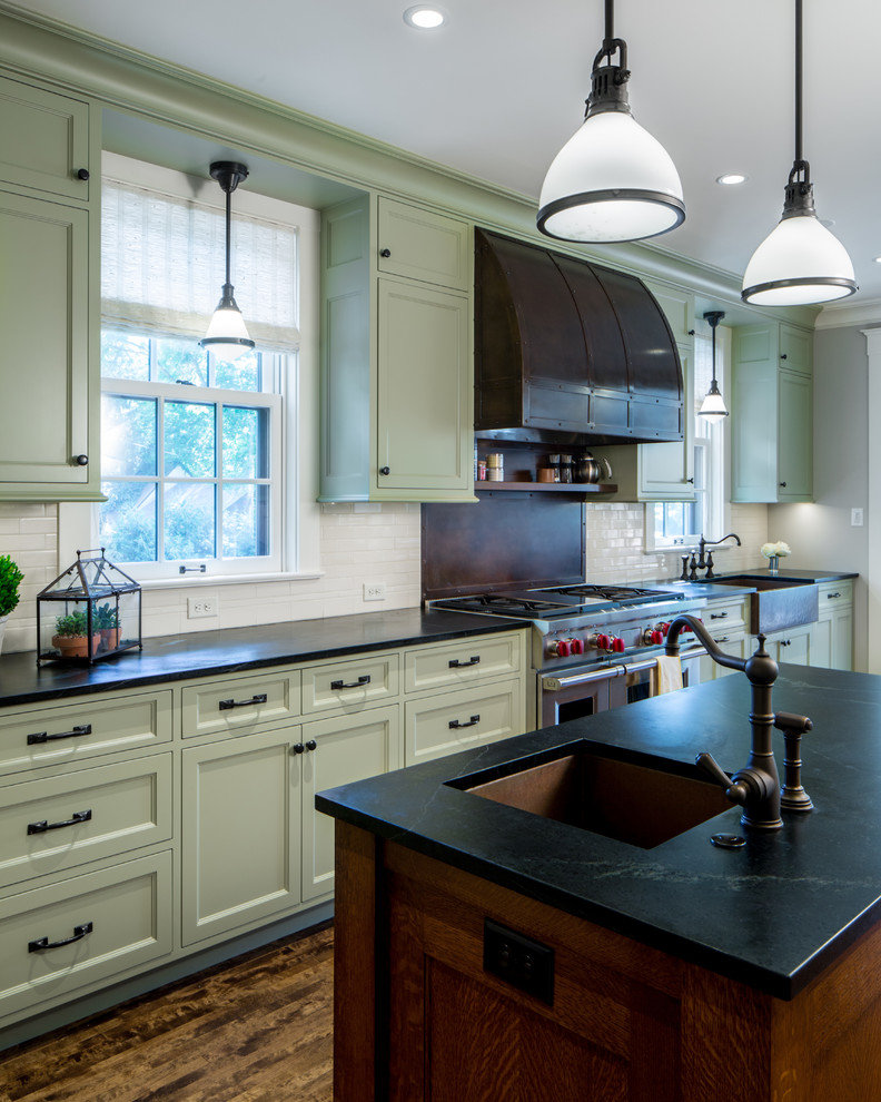 Design ideas for a large country galley open plan kitchen in Minneapolis with a farmhouse sink, recessed-panel cabinets, green cabinets, white splashback, ceramic splashback, dark hardwood floors, stainless steel appliances, soapstone benchtops and multiple islands.
