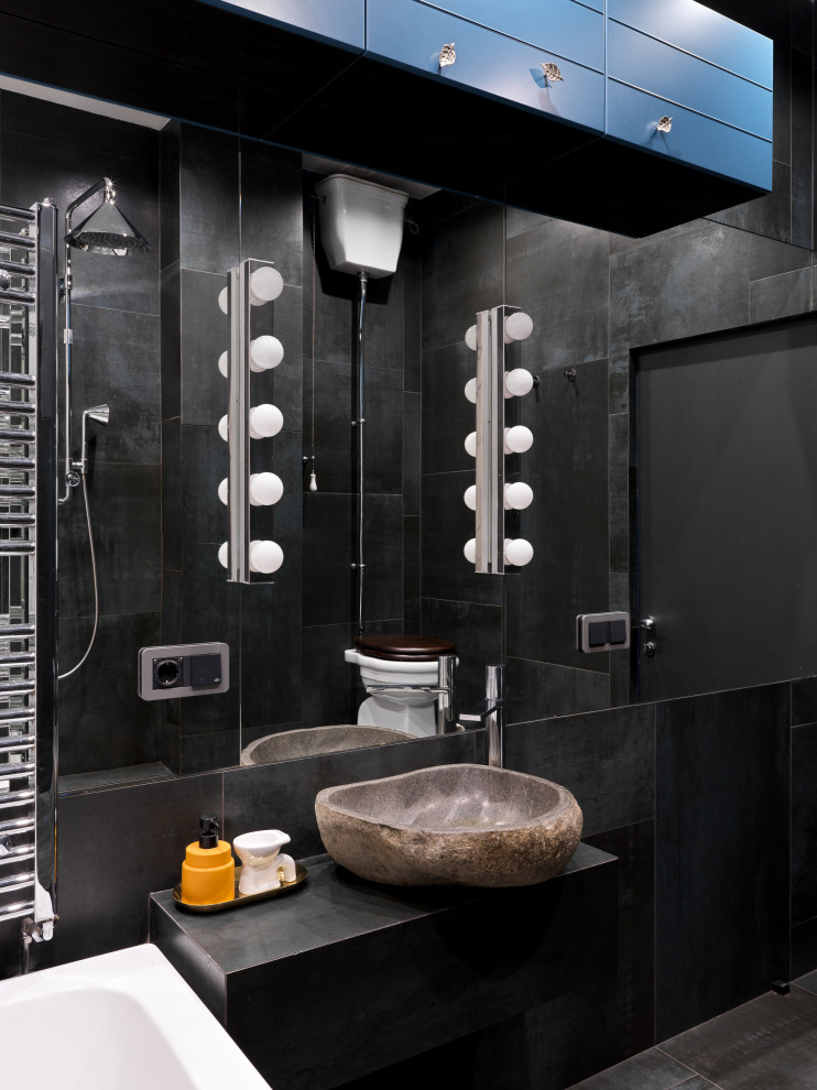 Свежая идея для дизайна: главная ванная комната среднего размера: освещение в стиле лофт с полновстраиваемой ванной, открытым душем, раздельным унитазом, серой плиткой, керамогранитной плиткой, черными стенами, полом из керамогранита, накладной раковиной, черным полом, открытым душем, тумбой под одну раковину и встроенной тумбой - отличное фото интерьера