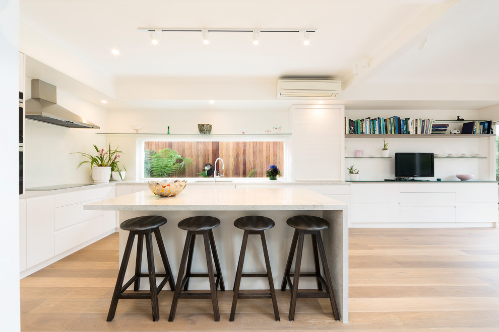 Contemporary l-shaped eat-in kitchen in Melbourne with an undermount sink, flat-panel cabinets, white cabinets, white splashback, window splashback, light hardwood floors, with island, beige floor and white benchtop.