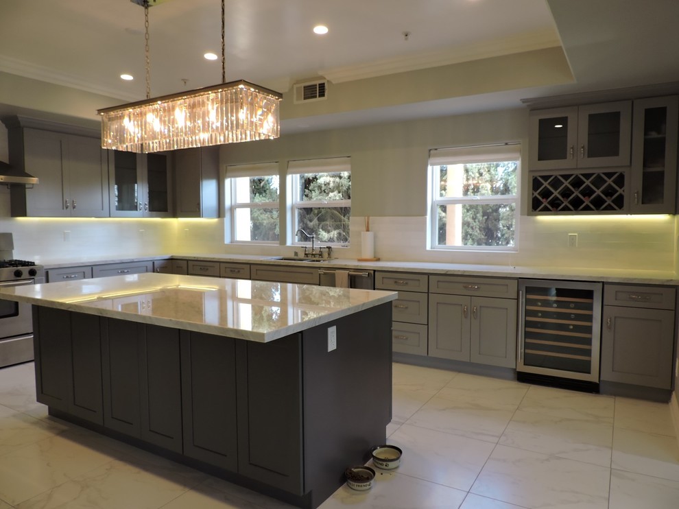 Large transitional u-shaped separate kitchen in Los Angeles with an undermount sink, shaker cabinets, grey cabinets, marble benchtops, white splashback, subway tile splashback, stainless steel appliances, marble floors, with island and brown floor.