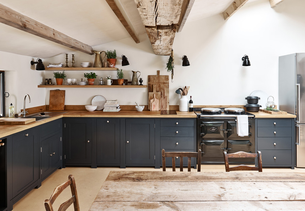 This is an example of a farmhouse l-shaped kitchen/diner with a built-in sink, shaker cabinets, grey cabinets, wood worktops, stainless steel appliances, no island, beige floors and beige worktops.