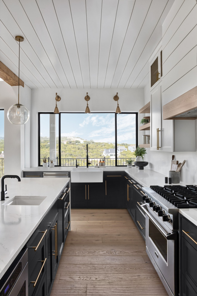 Mid-sized minimalist l-shaped light wood floor, beige floor and wood ceiling open concept kitchen photo in Austin with a farmhouse sink, shaker cabinets, black cabinets, quartzite countertops, white backsplash, marble backsplash, stainless steel appliances, an island and white countertops
