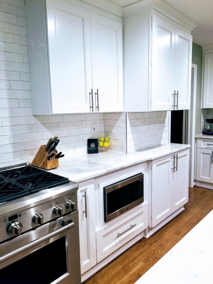 Large transitional u-shaped medium tone wood floor and brown floor enclosed kitchen photo in Miami with an undermount sink, shaker cabinets, white cabinets, quartz countertops, white backsplash, subway tile backsplash, stainless steel appliances, an island and white countertops