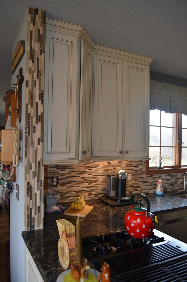 This is an example of a mid-sized country u-shaped eat-in kitchen in Detroit with an undermount sink, raised-panel cabinets, white cabinets, granite benchtops, brown splashback, matchstick tile splashback, stainless steel appliances, dark hardwood floors, a peninsula and brown floor.