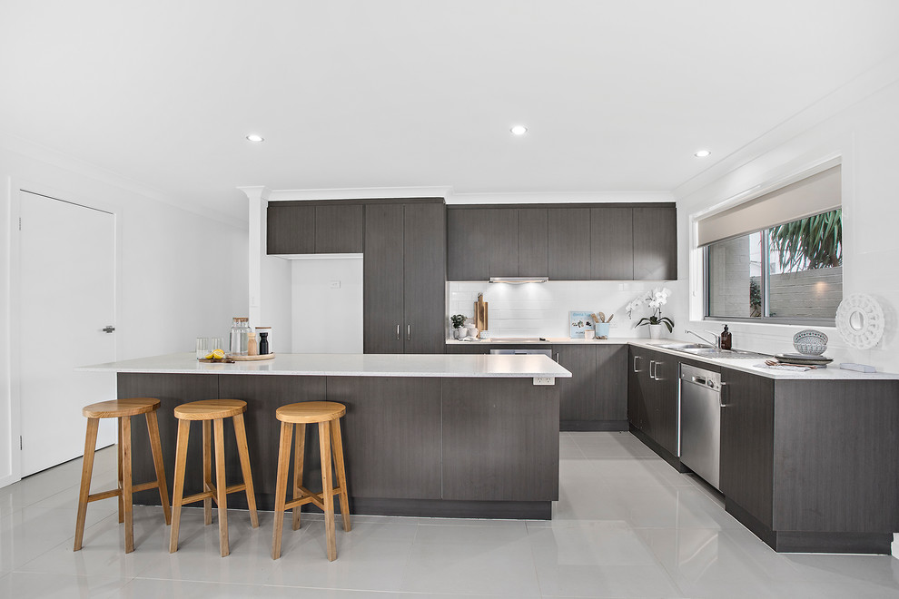 Inspiration for a beach style l-shaped kitchen in Other with a drop-in sink, flat-panel cabinets, grey cabinets, white splashback, stainless steel appliances, with island, grey floor and white benchtop.