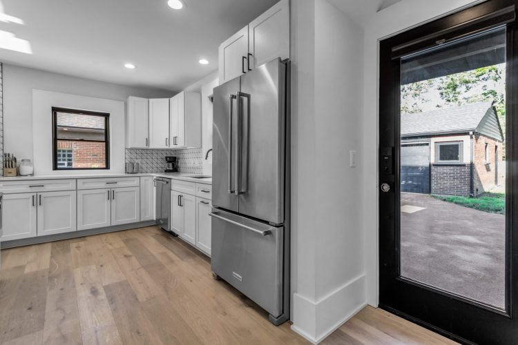 Mid-sized transitional l-shaped light wood floor and brown floor eat-in kitchen photo with an undermount sink, shaker cabinets, white cabinets, quartz countertops, white backsplash, ceramic backsplash, stainless steel appliances, an island and white countertops