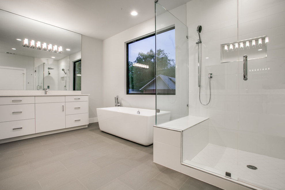 Large modern master bathroom in Dallas with flat-panel cabinets, white cabinets, a freestanding tub, a corner shower, white tile, ceramic tile, grey walls, porcelain floors, an undermount sink, solid surface benchtops, grey floor and a hinged shower door.