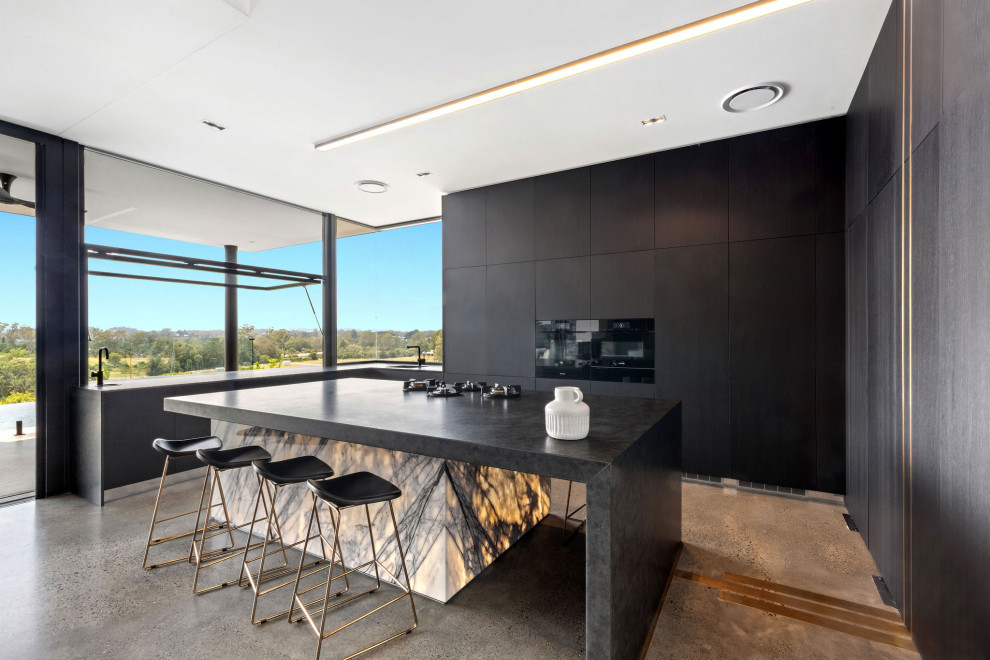 This is an example of a large contemporary u-shaped kitchen in Sunshine Coast with flat-panel cabinets, black cabinets, black appliances, concrete floors, with island, grey floor, an undermount sink, marble benchtops and black benchtop.