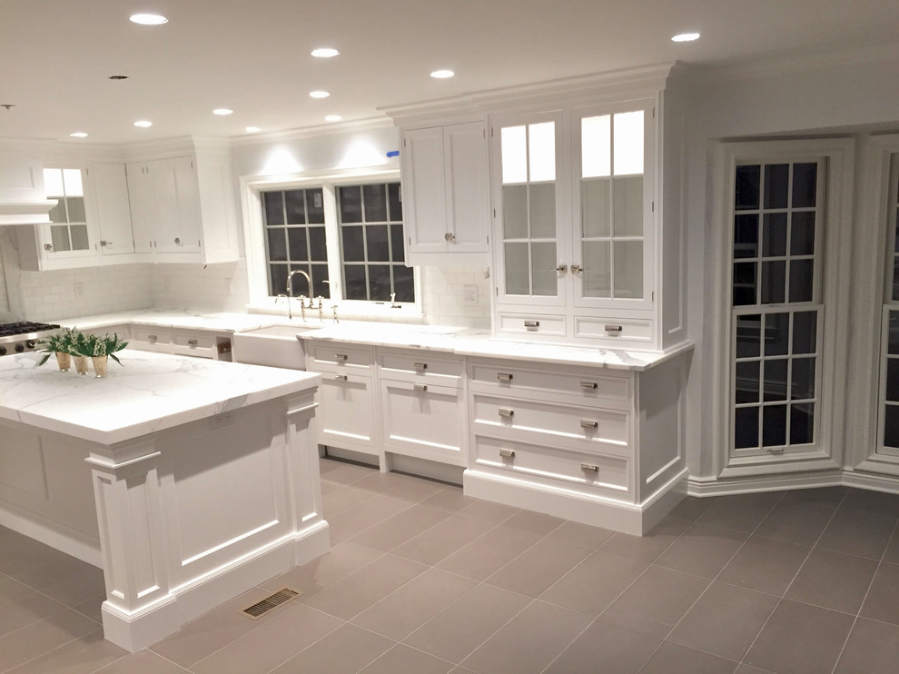 Large transitional l-shaped beige floor eat-in kitchen photo with a farmhouse sink, shaker cabinets, white cabinets, white backsplash, stainless steel appliances and an island