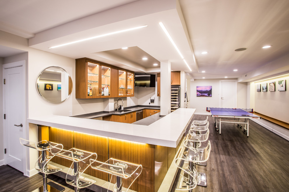 Large modern u-shaped seated home bar in New York with an undermount sink, glass-front cabinets, medium wood cabinets, solid surface benchtops, white splashback, painted wood floors and brown floor.