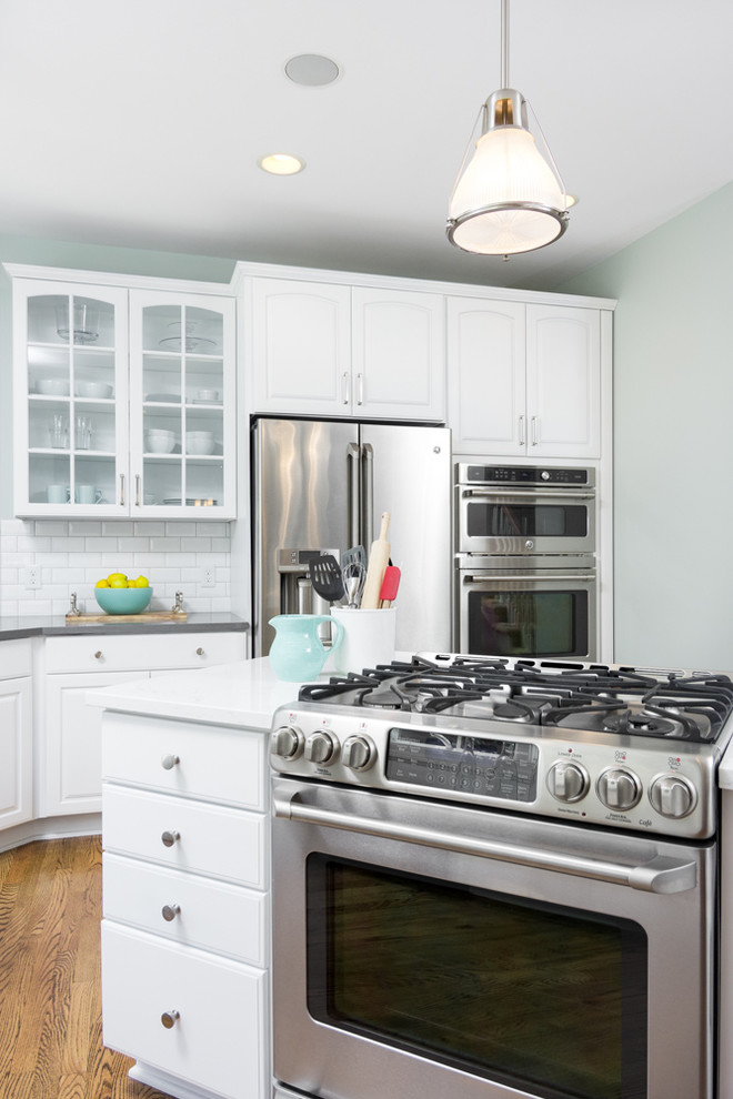 Eat-in kitchen - large transitional u-shaped medium tone wood floor and brown floor eat-in kitchen idea in Detroit with an undermount sink, raised-panel cabinets, white cabinets, quartz countertops, white backsplash, ceramic backsplash, white appliances and an island