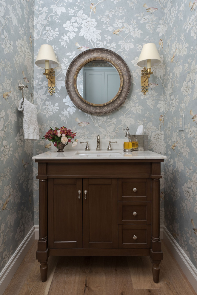 Inredning av ett klassiskt litet vit vitt toalett, med möbel-liknande, skåp i mörkt trä, ljust trägolv, ett undermonterad handfat och marmorbänkskiva