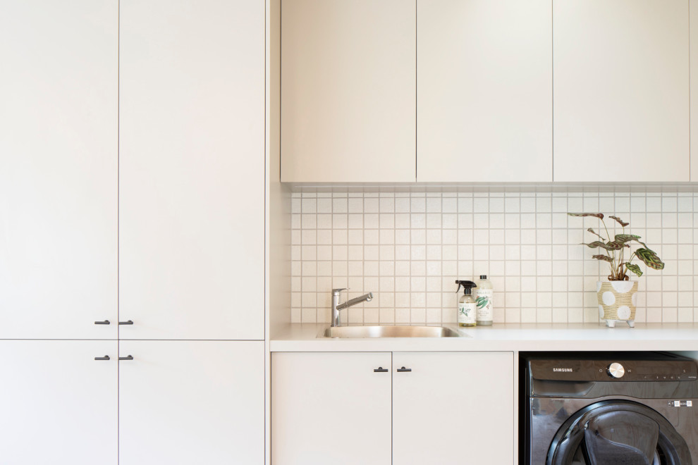 Photo of a small contemporary single-wall utility room in Melbourne with a drop-in sink, flat-panel cabinets, beige cabinets, laminate benchtops, white splashback, mosaic tile splashback, beige walls, concrete floors, a side-by-side washer and dryer, grey floor, beige benchtop, wood and wood walls.