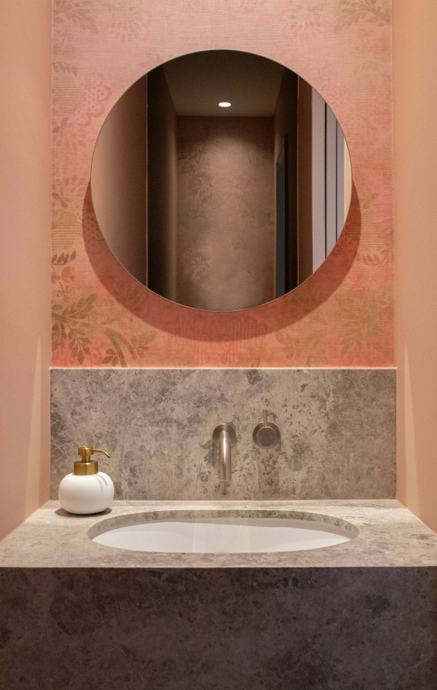 Diseño de aseo flotante pequeño con sanitario de pared, paredes rosas, suelo de baldosas de porcelana, lavabo bajoencimera, encimera de piedra caliza, suelo gris, encimeras grises y papel pintado