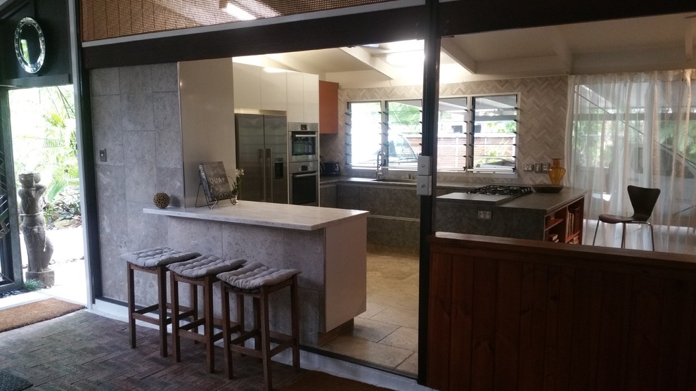Design ideas for a mid-sized eclectic u-shaped home design in Darwin with a drop-in sink, flat-panel cabinets, blue cabinets, solid surface benchtops, grey splashback, mosaic tile splashback, stainless steel appliances, slate floors and multiple islands.
