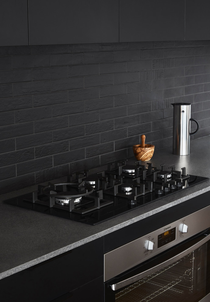 Design ideas for a mid-sized modern galley open plan kitchen in Sydney with a double-bowl sink, flat-panel cabinets, black cabinets, quartz benchtops, black splashback, ceramic splashback, black appliances, light hardwood floors, with island and grey benchtop.