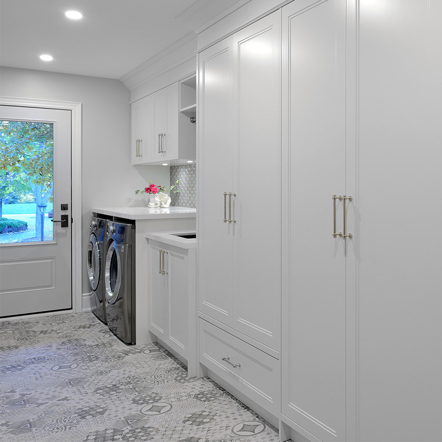 Photo of a large transitional single-wall utility room in Toronto with an undermount sink, recessed-panel cabinets, white cabinets, quartz benchtops, grey splashback, glass tile splashback, grey walls, porcelain floors, a side-by-side washer and dryer and white benchtop.