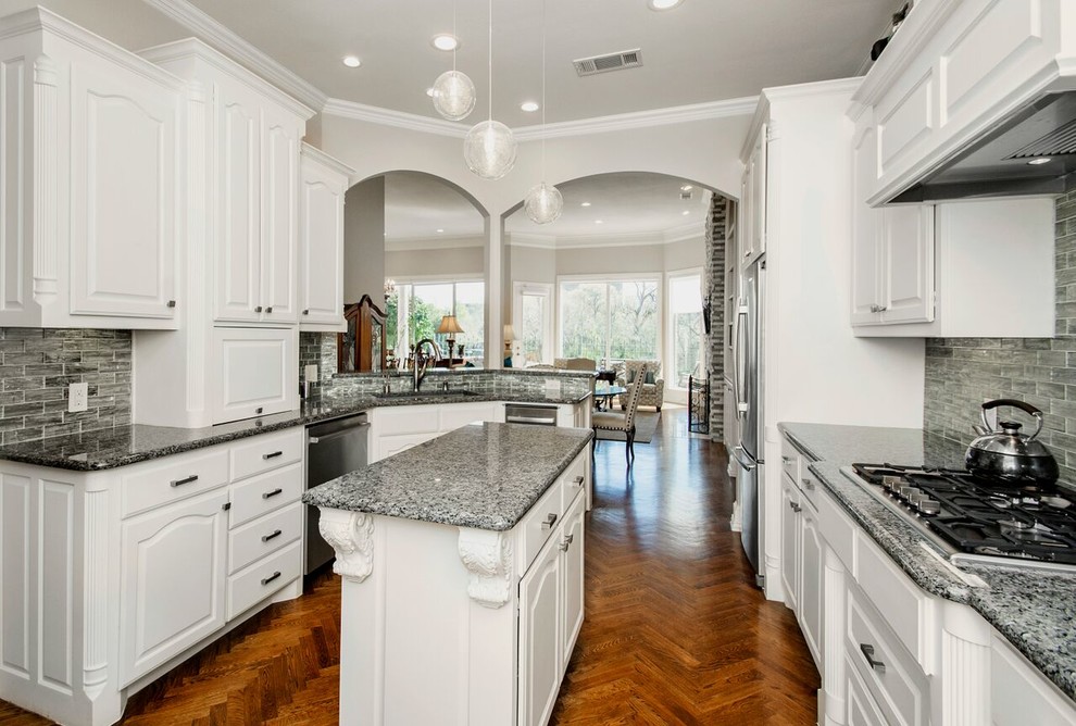 This is an example of a mid-sized transitional u-shaped kitchen pantry in Dallas with an undermount sink, raised-panel cabinets, white cabinets, quartz benchtops, metallic splashback, glass tile splashback, black appliances, medium hardwood floors, with island, brown floor and grey benchtop.