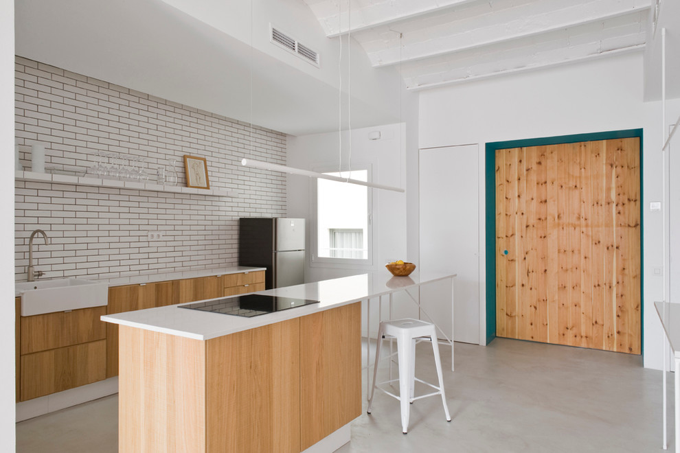 Inspiration for a mid-sized scandinavian galley separate kitchen in Barcelona with a farmhouse sink, flat-panel cabinets, light wood cabinets, white splashback, subway tile splashback, concrete floors, with island and solid surface benchtops.