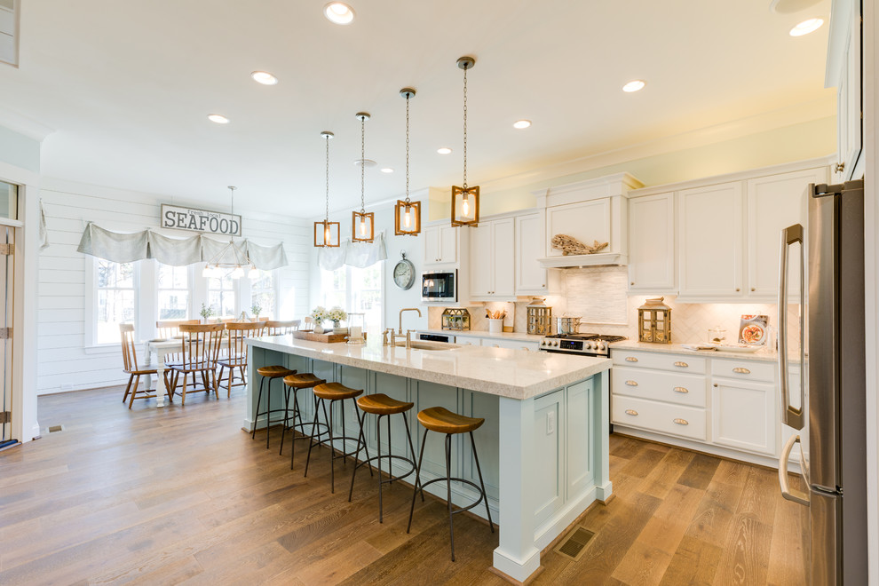 Design ideas for a large beach style l-shaped open plan kitchen in Other with a farmhouse sink, shaker cabinets, white cabinets, quartzite benchtops, white splashback, marble splashback, stainless steel appliances, medium hardwood floors, with island and brown floor.