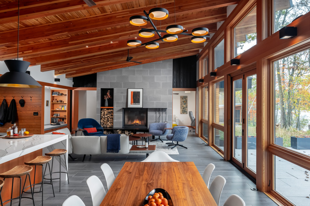 This is an example of a large country open concept living room in Minneapolis with multi-coloured walls, porcelain floors, a standard fireplace, a concrete fireplace surround, no tv, grey floor, exposed beam and wood walls.