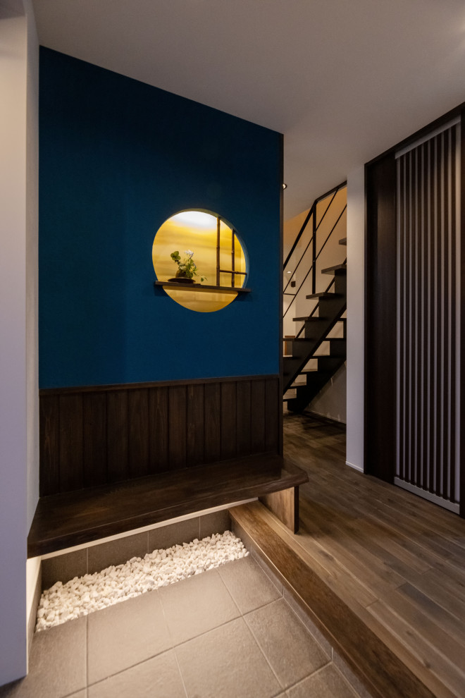 На фото: узкая прихожая среднего размера с синими стенами, полом из известняка, одностворчатой входной дверью, входной дверью из дерева среднего тона, серым полом, потолком с обоями и деревянными стенами с
