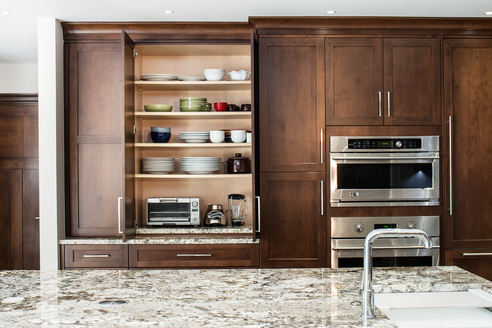 Example of a large transitional ceramic tile and beige floor eat-in kitchen design with an undermount sink, shaker cabinets, brown cabinets, granite countertops, white backsplash, glass tile backsplash, stainless steel appliances and an island
