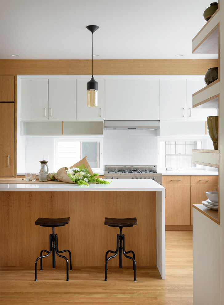 This is an example of a contemporary kitchen in Seattle with flat-panel cabinets, medium wood cabinets, window splashback, stainless steel appliances, light hardwood floors, with island, beige floor and white benchtop.