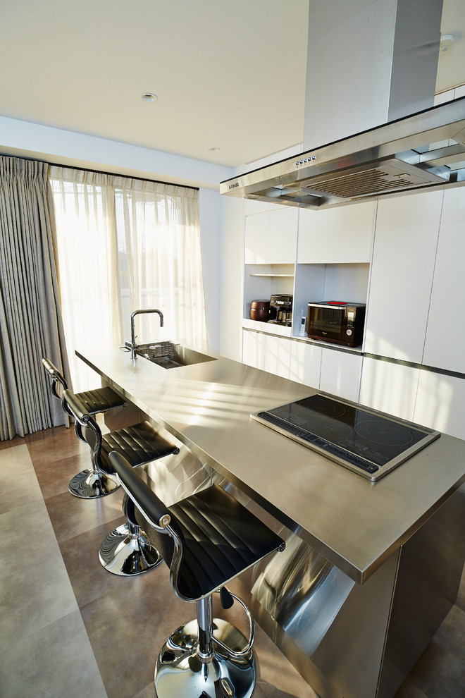 Contemporary single-wall open plan kitchen in Osaka with an integrated sink, flat-panel cabinets, white cabinets, stainless steel benchtops, white splashback, stainless steel appliances and with island.
