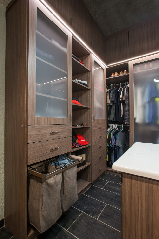 This is an example of a mid-sized modern men's walk-in wardrobe in Denver with flat-panel cabinets, medium wood cabinets, ceramic floors, grey floor and vaulted.