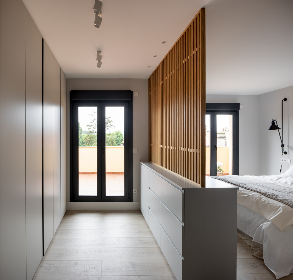 Foto de dormitorio principal y blanco y madera moderno grande sin chimenea con paredes grises, suelo laminado y suelo marrón