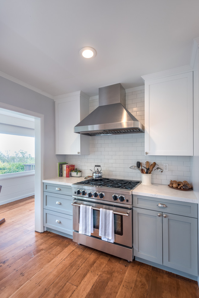This is an example of a mid-sized country eat-in kitchen in San Francisco with a farmhouse sink, shaker cabinets, white cabinets, white splashback, ceramic splashback, medium hardwood floors and no island.